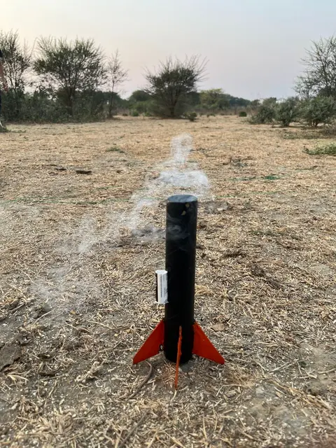 What remained of Homi Shatam I, a black body tube with orange fins, standing on the launch pad in a dry field, smoke still drifting behind it.