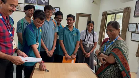 Students and two teachers stand around a table as an agreement is signed.