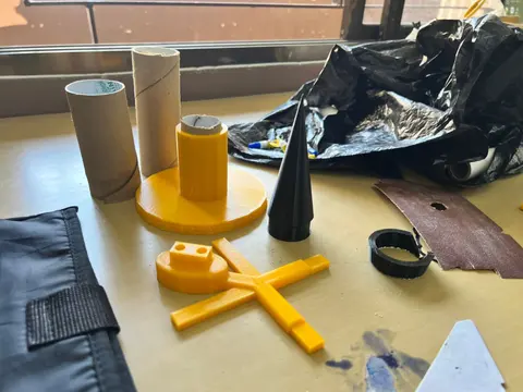 Yellow 3D-printed parts, cardboard tubes and a black nose cone on a table.
