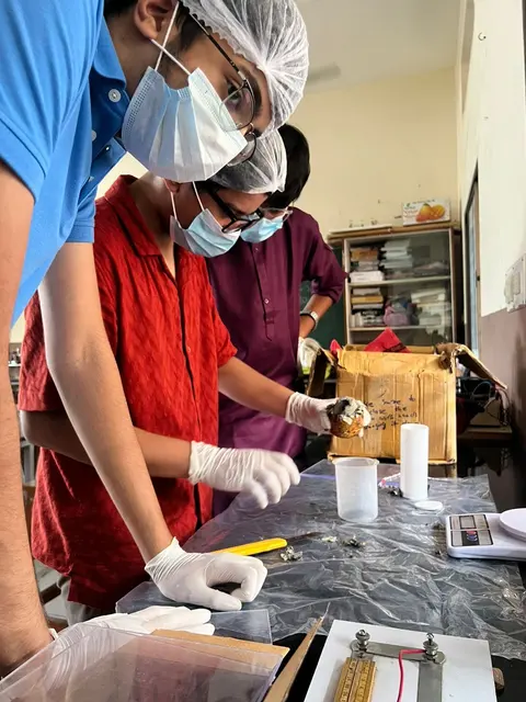 Team members in masks, gloves and hairnets work at a table with plastic containers.