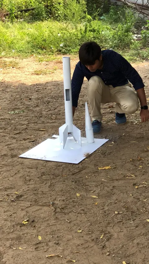 A team member crouches beside SRM, still unpainted white, standing on a white launch board in a dirt field.